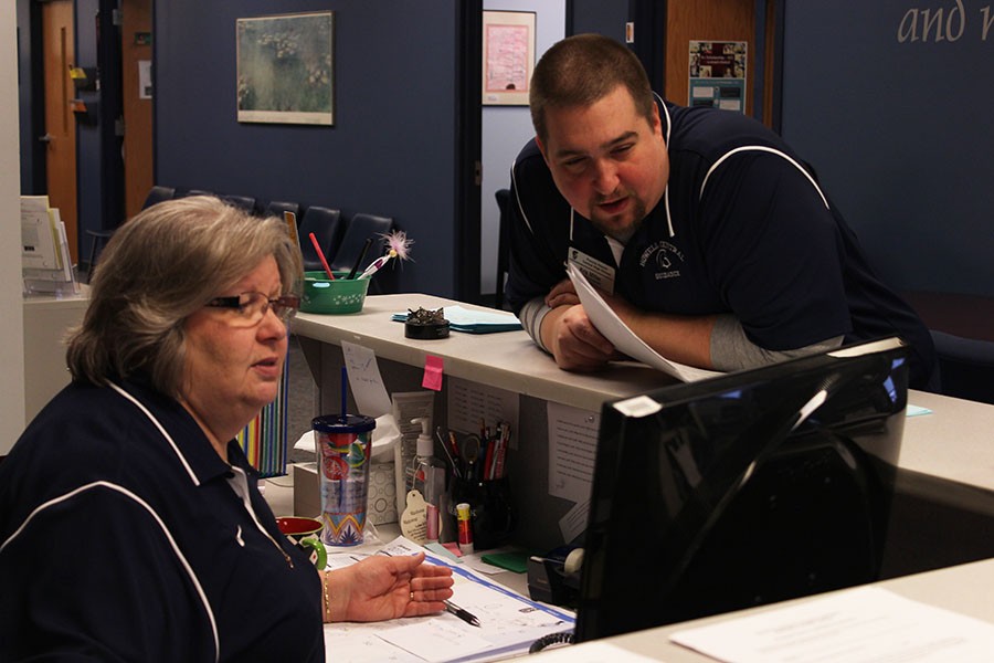 Guidance counselor Mr. Miller and guidance secretary Mrs. Lipin discuss something on the computer screen.  They are preparing the schedules for next years students.