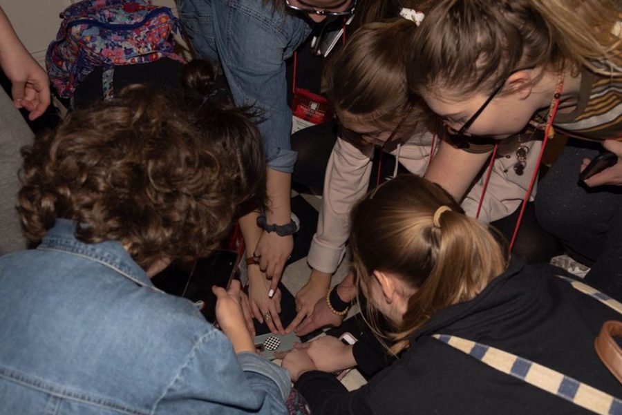 The theatre kids gather around a phone and touch the plaid pop socket for good luck. Evidently this worked because Troupe 5743 did very well at Thescon this year. 