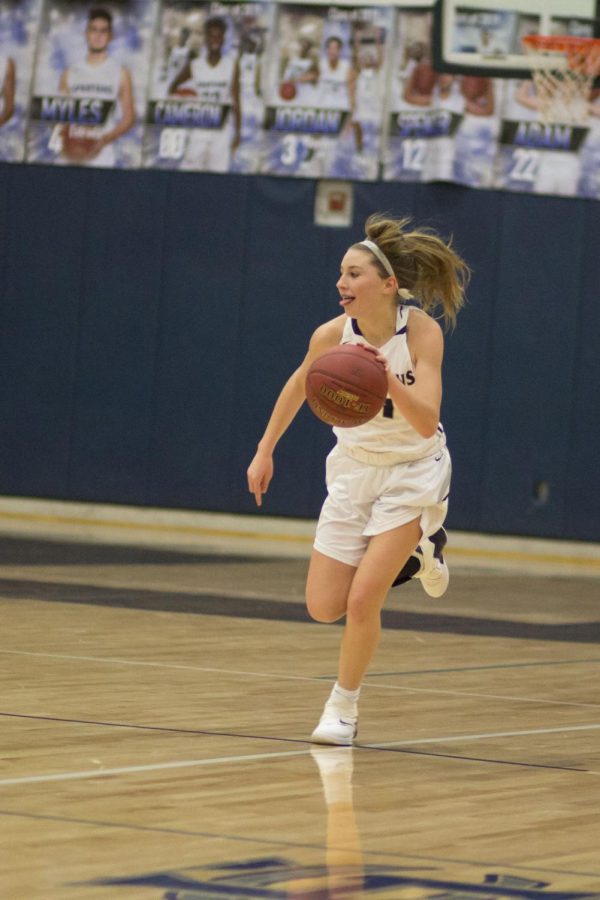 Gracie Stugart drives down the court, tongue sticking out, displaying her passion and love for the game. her enthusiasm is clear as she looks for one of her teammates to pass the ball to. 