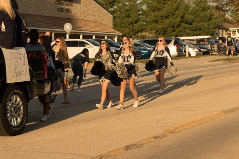 The varsity cheerleads walk at the homecoming parade showing their school spirit as they smile at children
