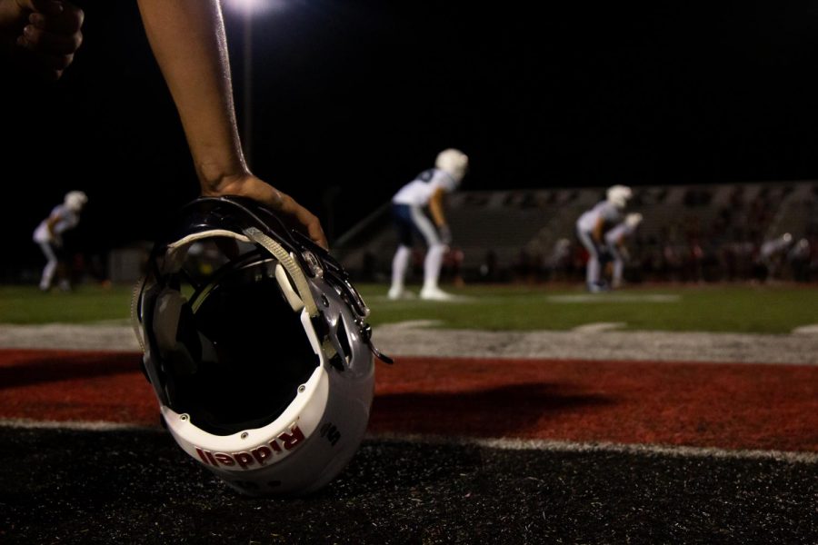 A football player crouches next to his helmet as he prepares for the game. 