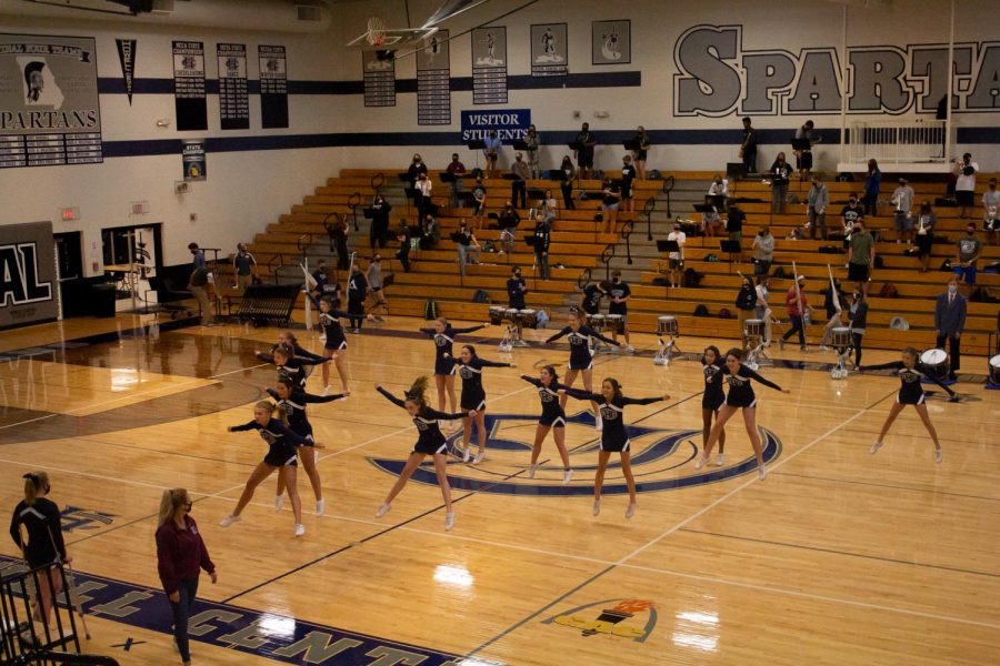 The Varsity Cheerleaders perform at the schools first ever virtual pep assembly while the band and color guard attentively watch on Sept. 23. The gym seemed empty as masked band members social distanced, using up all of the space in the  bleachers. The event was live-streamed into classrooms so they could participate in the spirit week event.