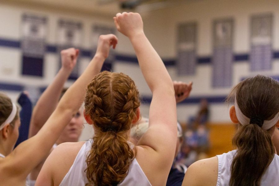 The varsity girls basketball team stands together with their fists raised in the air. 