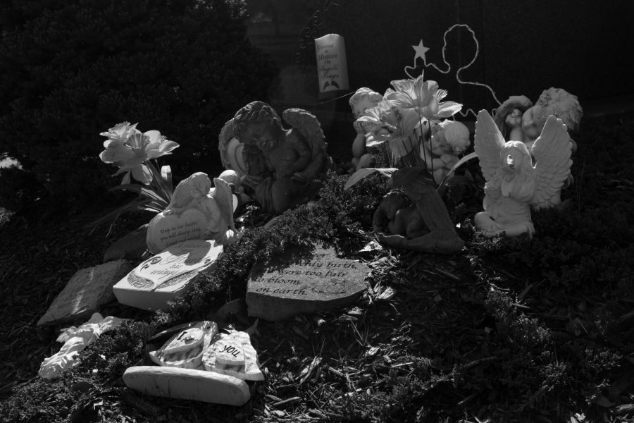 Statues of angels and carved stones are set out to commemorate the loss of a person who was close to many people. The fresh flowers show that someone has visited recently to recall their loving memories.