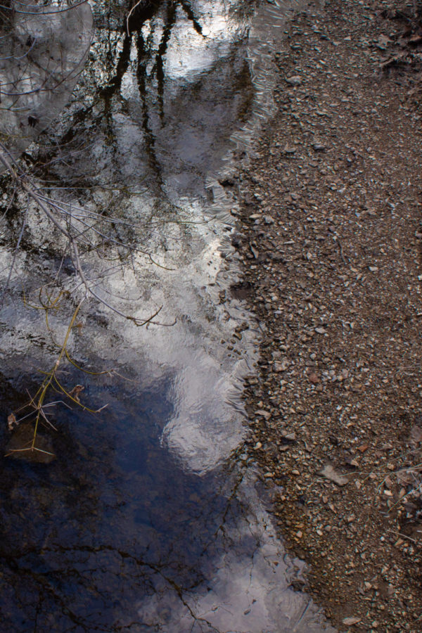 The sky is reflected in the icy water of a stream in a woods. Sometimes, the best way to look up is simply to look down.