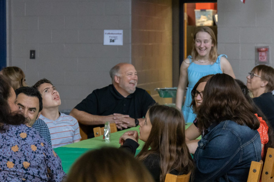 Students and parents talk and laugh together at tables.