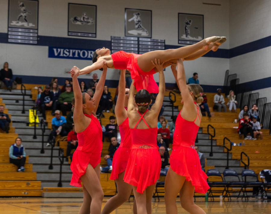 Members of the dance team elevate their fellow teammate off of the ground, as she basks in the lights of the gym. 