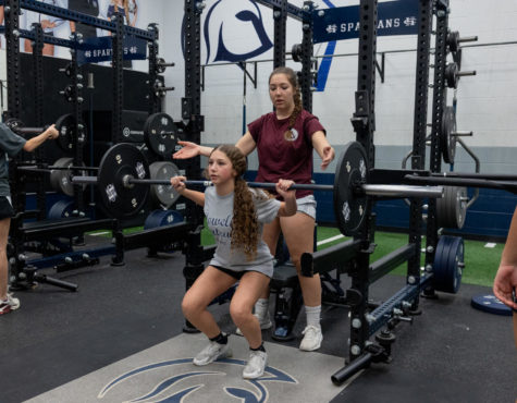 Senior Gianna Bruenning assists an underclassman with her squat rep. Teammate Delaynie Brown mentioned how winter workouts are a glimpse into the future of their team. Were...getting a look at what our program is gonna look like that year.