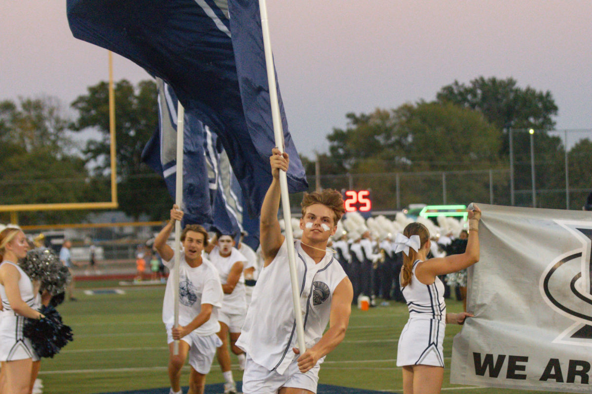 Student section leader Nate Rush runs through the tunnel of cheerleaders with a flag moments before the football team charges through the sign.