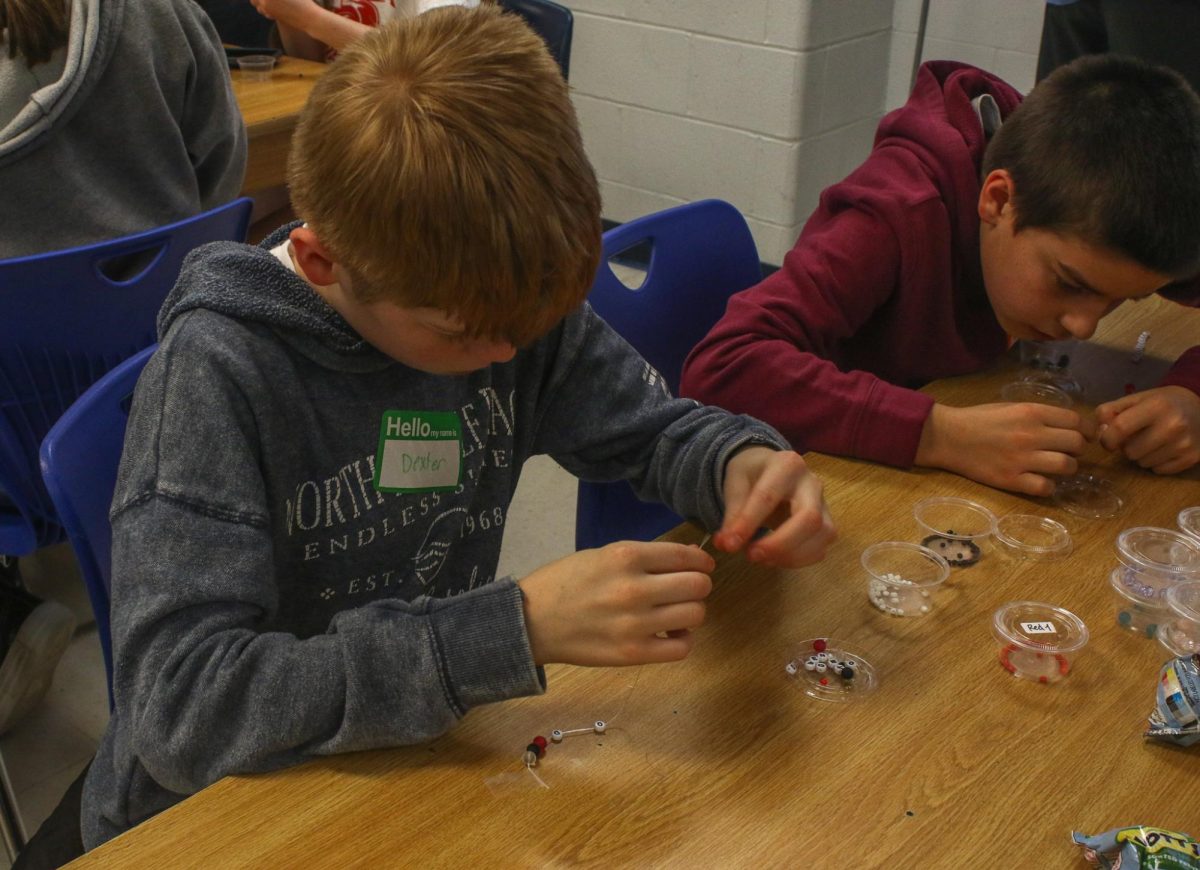 The middle school student feeding his bracelet string through the bead to assemble his friendship bracelet. 