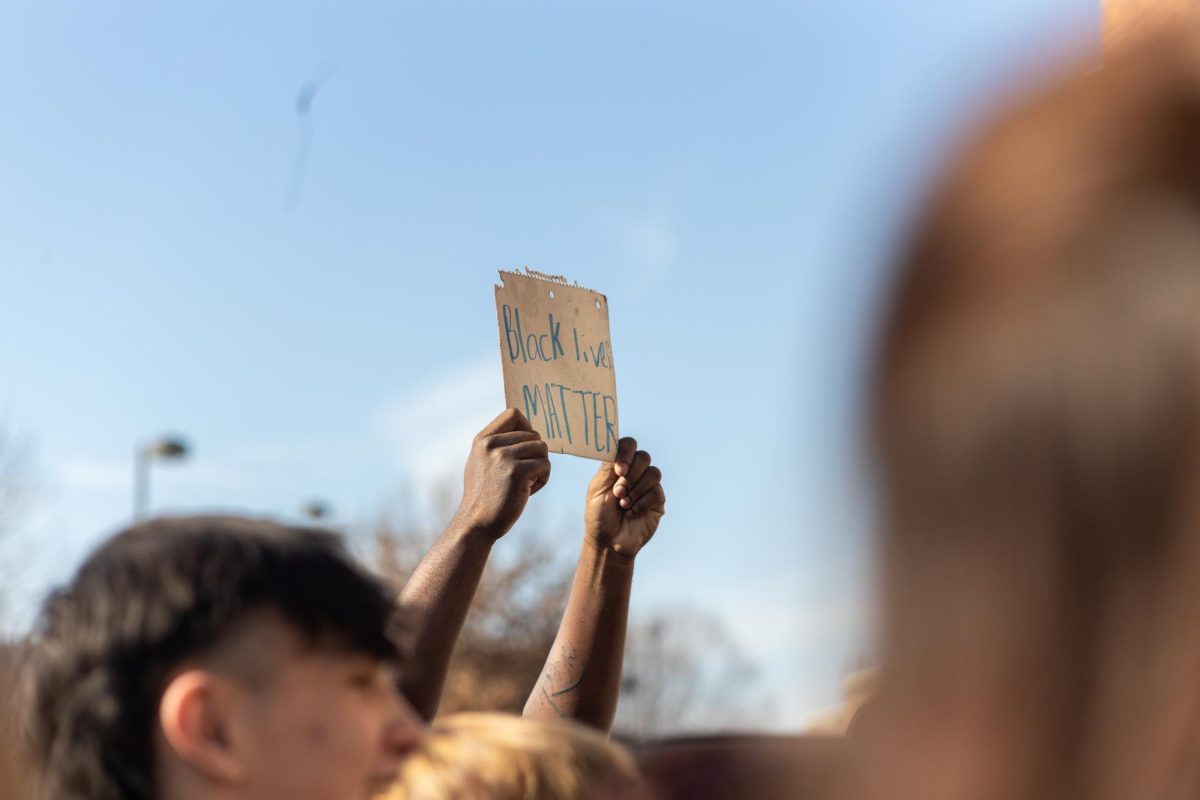 Student holds up a makeshift sign made of a notebook backing. 