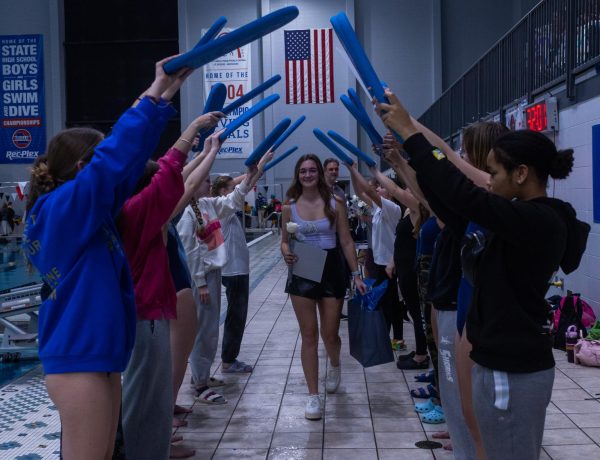 Holding her flower and gift bag, senior Finley Brunner walks through the tunnel of swim boards held up by her teammates. Brunner was captain for her last year on the team. 