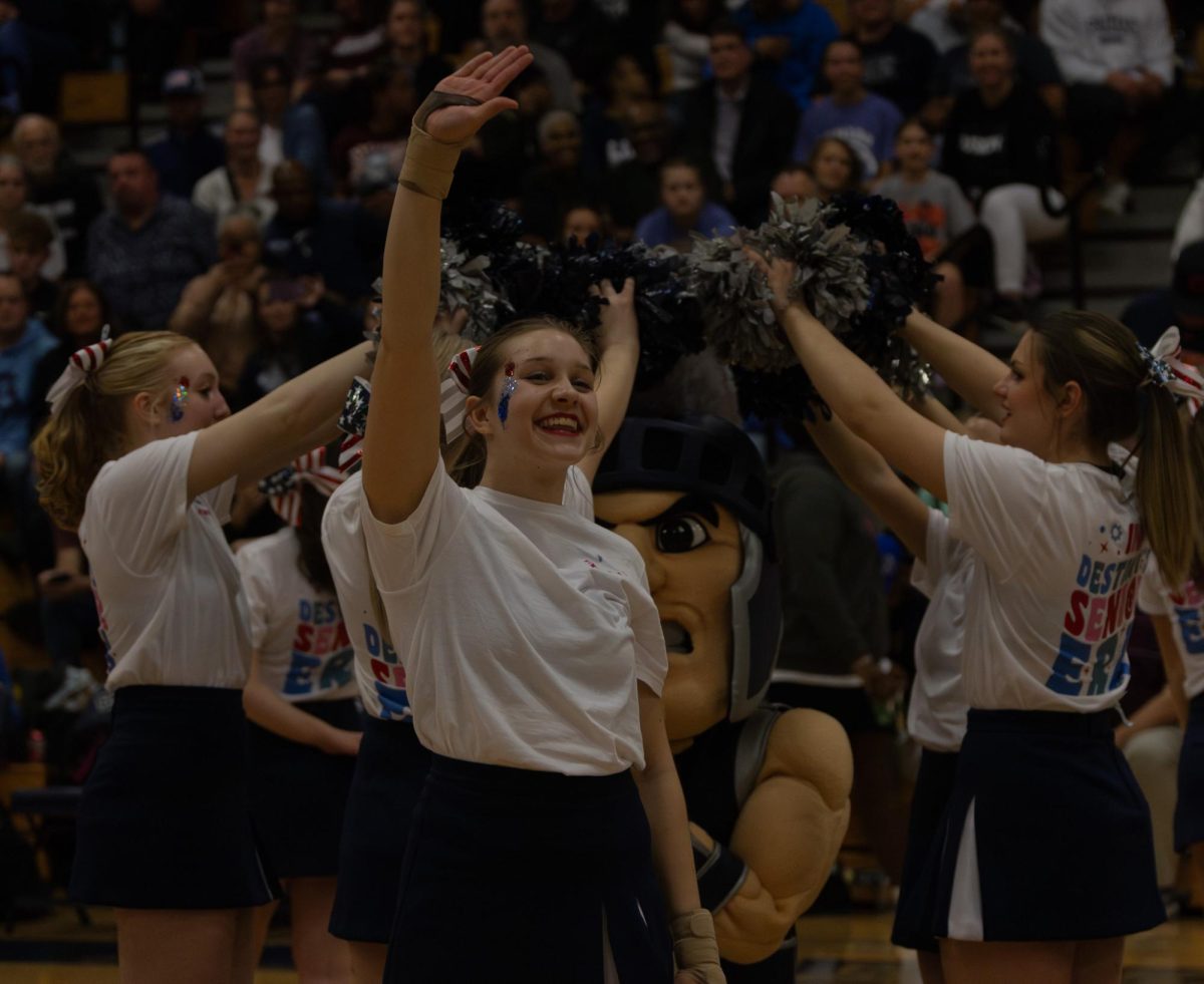 Junior cheerleader Violet Gallagher waves to the audience before completing her tumbling pass across the court while she and her varsity team perform at halftime.
