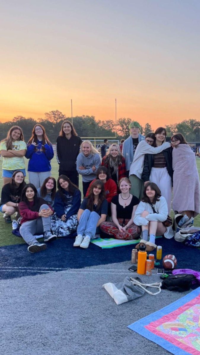 The sun sets as senior Sophie Shore, seated in the bottom row, and her friends take a photo on the football field at the end of the 2022-23 school year. Many of the students in the photos graduated, so theyre trying to make the most of their time left together. Photo courtesy of Sophie Shore.