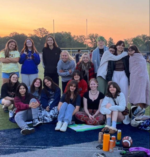 The sun sets as senior Sophie Shore, seated in the bottom row, and her friends take a photo on the football field at the end of the 2022-23 school year. Many of the students in the photos graduated, so theyre trying to make the most of their time left together. Photo courtesy of Sophie Shore.