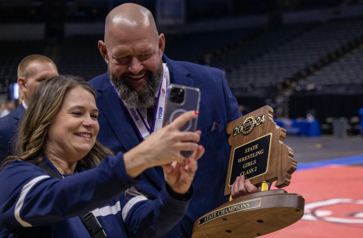 Coach+Kurt+Kruse+holding+the+team+state+champion+award+while+leaning+in+for+a+photo+after+the+girls+wrestling+team+won+the+state+championship+on+Feb.+24.