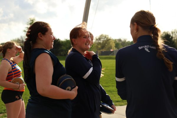 Juniors, Kat Mann and Bailey Adkerson, along with sophomore, Cooper Rowse stand around the discus arena as they wait their turn to practice throwing. Kat Mann laughs with the wind in her hair.