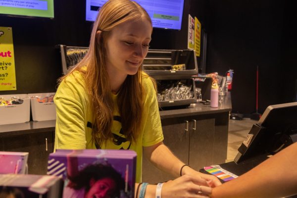 Junior Layci Kenoyer putting on an entrance bracelet on a kid at the Urban Air Trampoline Park. Working at the front desk station, she greets guests and helps with questions and concerns.