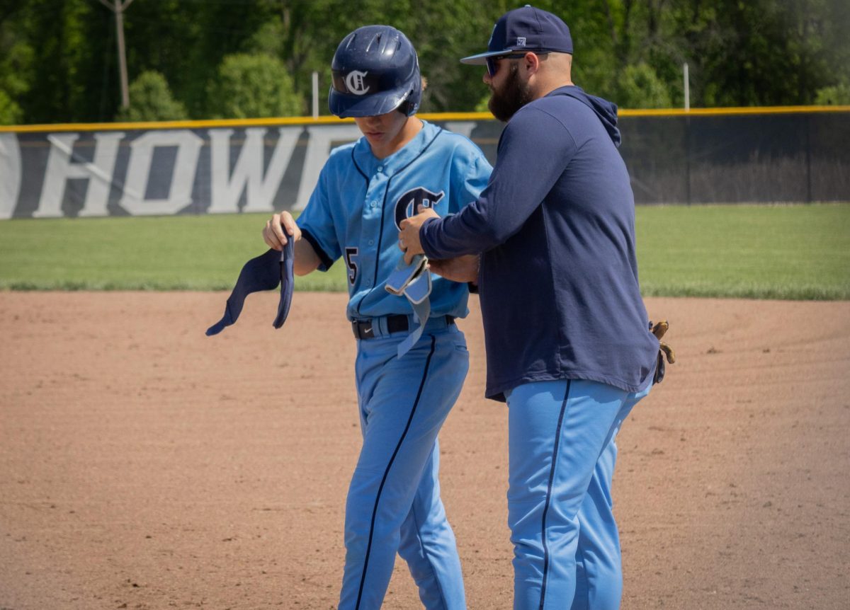 On May 4, freshman Carter Radeke hands his batting glove to one of his coaches while they talk about his next move and he puts on his sliding mitt during the Central vs Eureka game. 