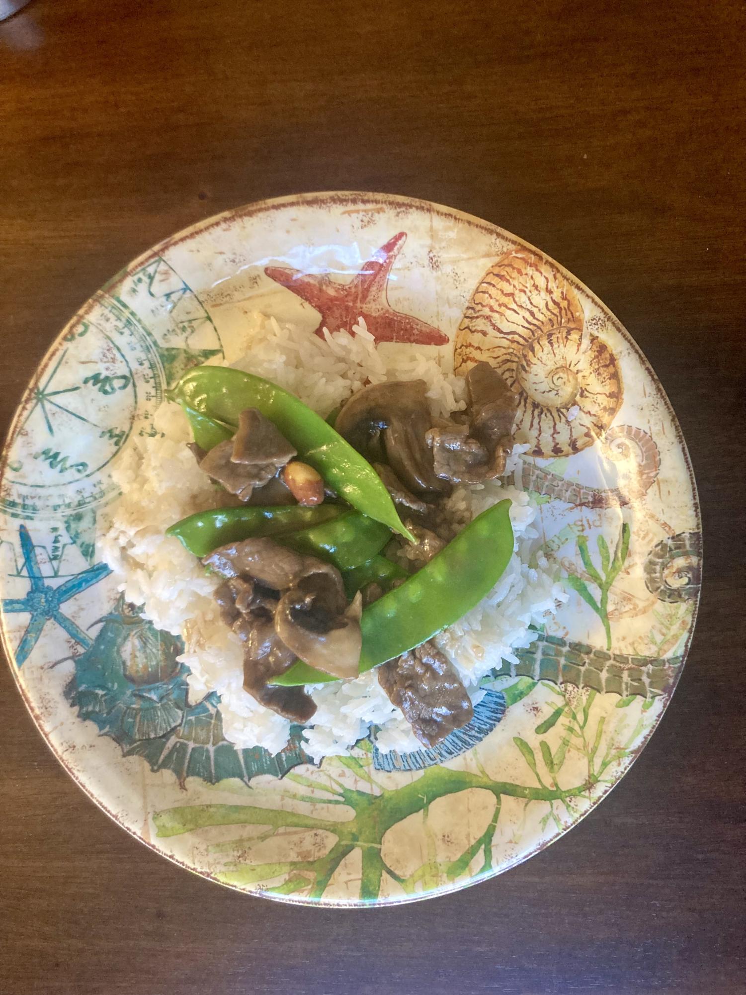 Beef stir fry over rice with mushrooms and pea pods.