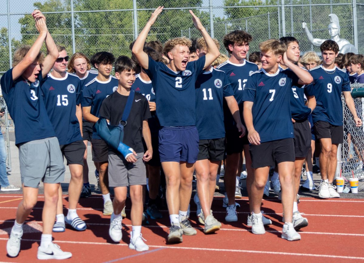 Walking out on the track, sophomore Carter Radeke throws his hands in the air and yells with his teammates. Radeke did this to try and hype up the varsity boys soccer team as they were walking in front of their friends and family.