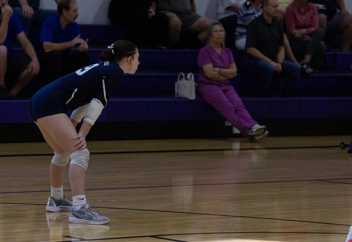 Freshman Andi Hopson is standing with her hand resting on her knees. Hopson is observing the other team, waiting for the ball to pass back over the net.