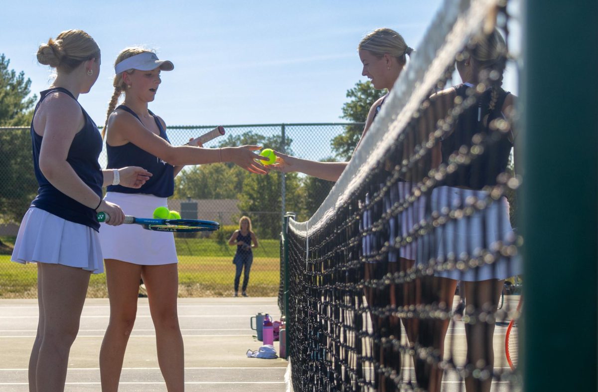 Meeting the other team at the net, sophomore Isabel Black and her doubles partner grab the ball from her opponents. Trading the tennis balls signals the beginning of a new set. 