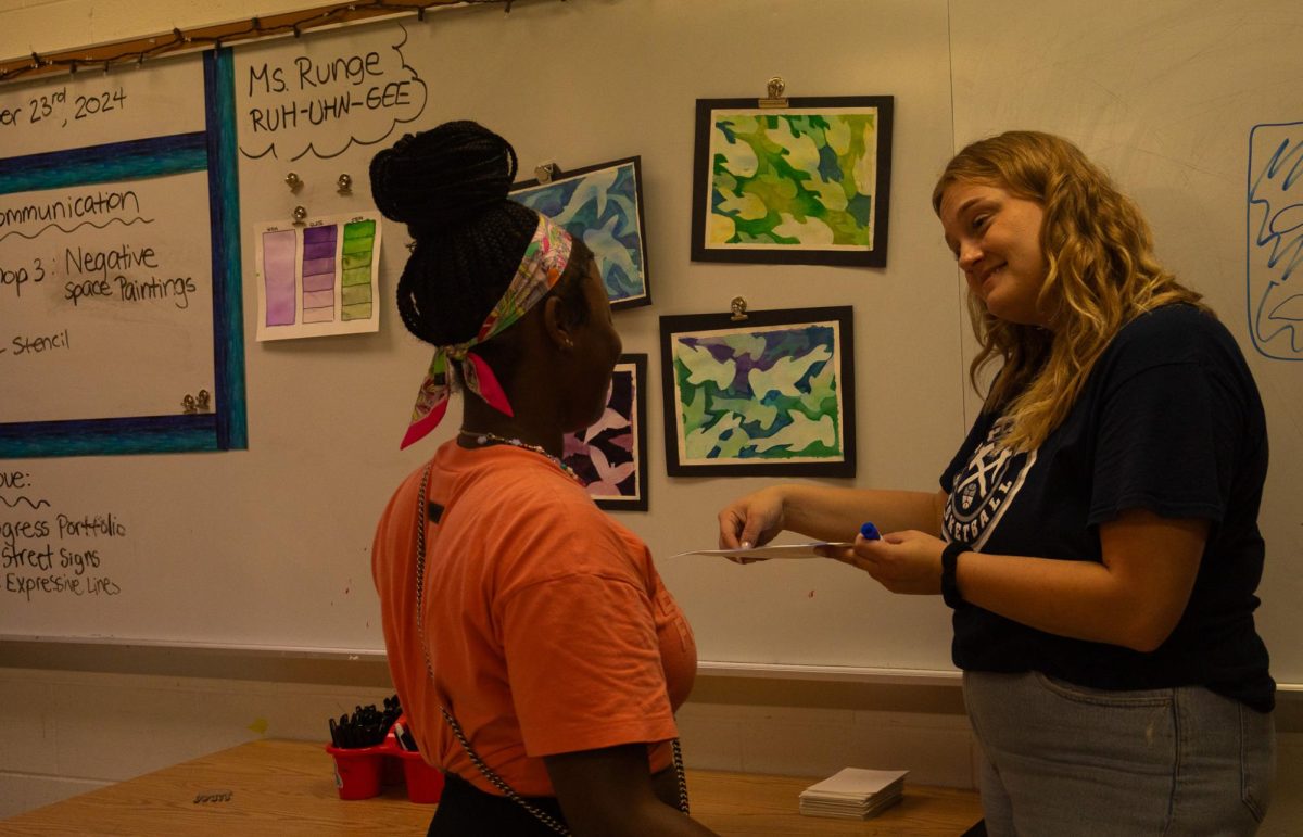 Ms. Ashley Runge discusses the organization of the watercolor painting with a student. The project was intended to teach students about the meaning of negative space and when to use it. 
