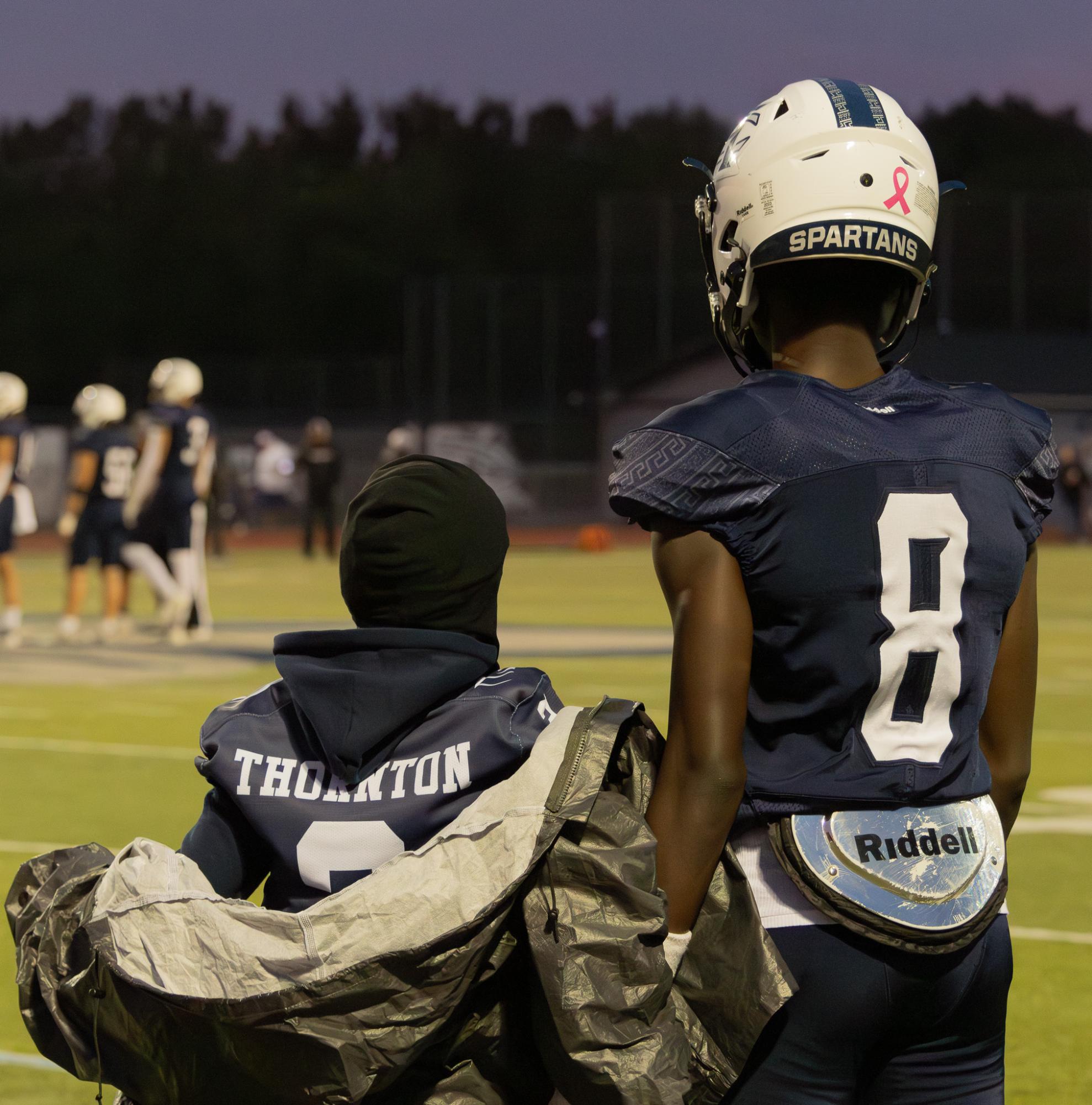 Before the game begins, junior Don Thornton stands next to his little brother who is a Junior Spartan over at Saeger. The Junior Spartans stood next to the team on the sidelines and helped keep the team hydrated. 