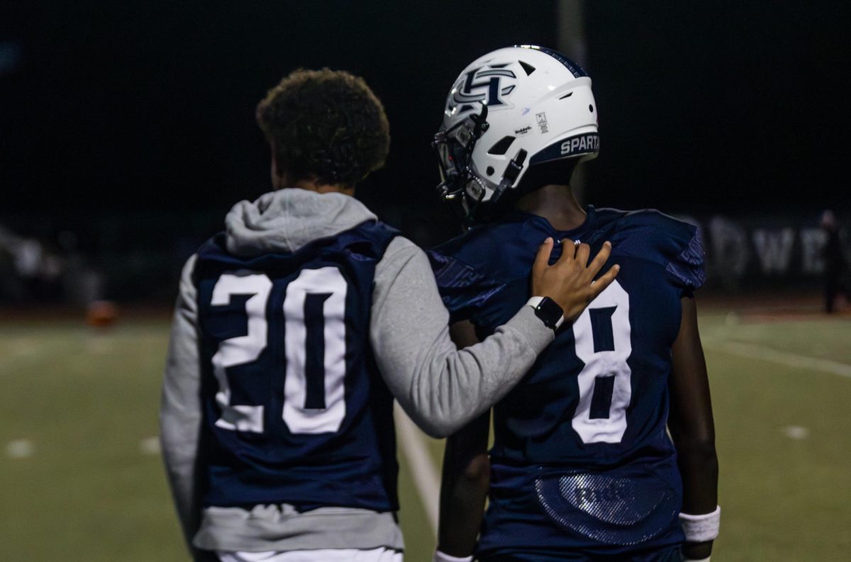 Junior Cameron Jordan puts his arm around his teammate junior Don Thornton in support as he sits on the bench. Although Jordan is not able to play this season, he still attends all games and practices to support his fellow teammates.
