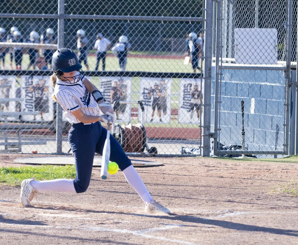 Junior Savanna Cohen swings her bat and makes contact with the ball as her feet slide while bracing against the impact. Cohen’s hit was successful so she sprinted forward and rested at first base.