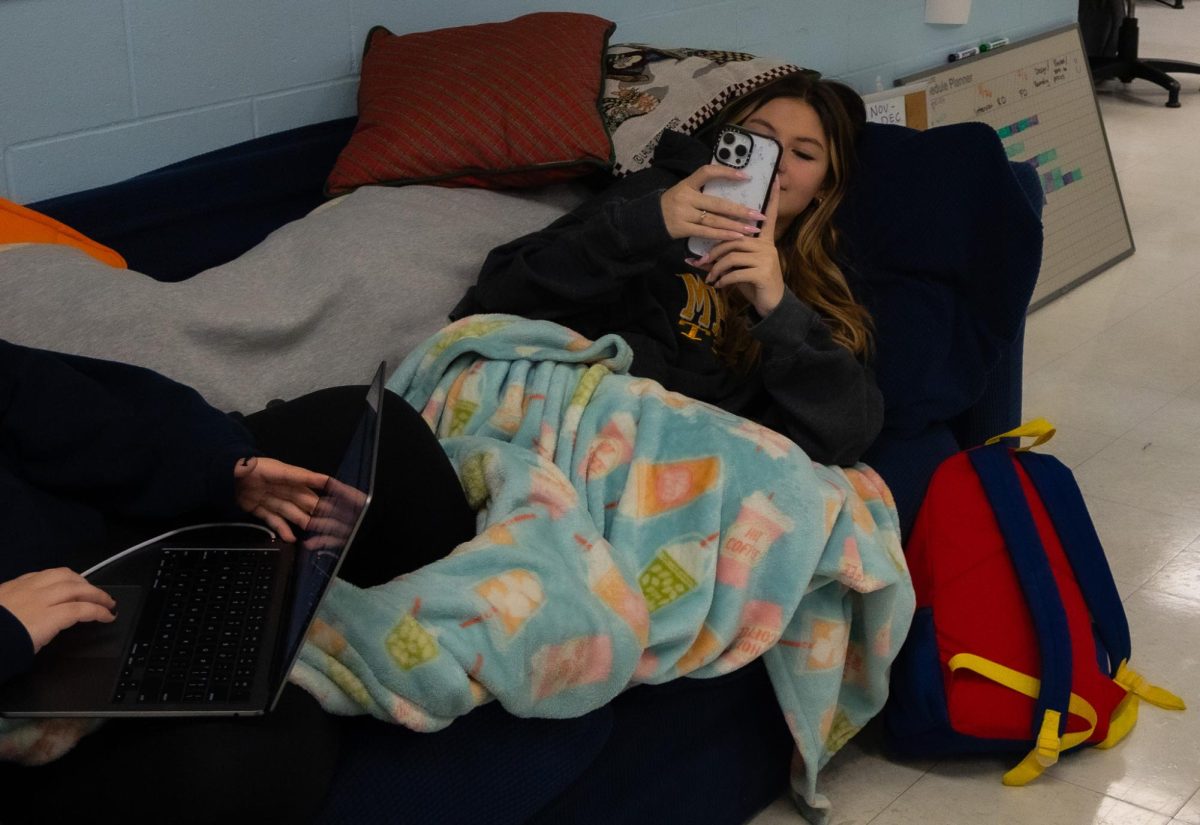 Senior Lillian Seithel lays on a classroom couch, scrolling through her phone. Since students must wake up early to start school at 7:20 am, some students feel tired during the first few hours of their day.