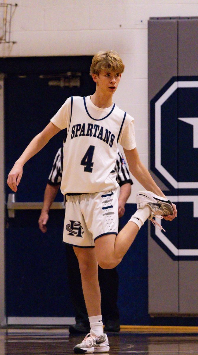 Freshman Tate Hackmann wipes the bottom of his shoe between plays to prevent slipping on the court. The Spartans took this moment to prepare on the court while St. Dominic finished their timeout.