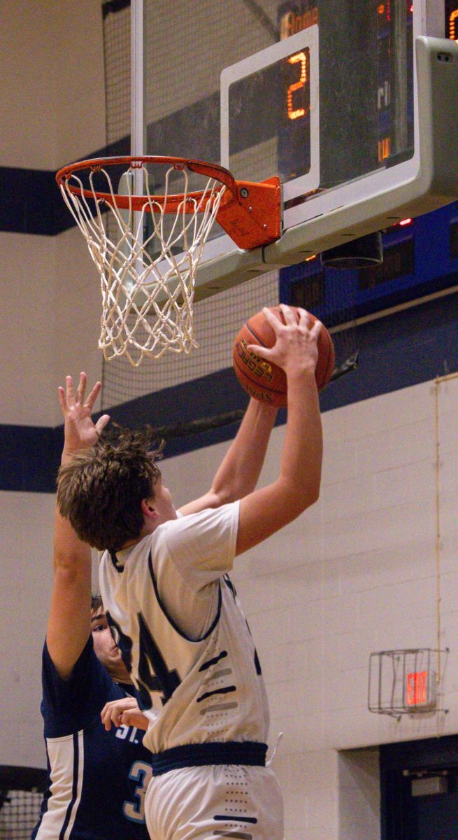 Dylan Bulva grabs an offensive rebound over a defender’s outstretched hand. After his teammate missed a shot, Bulva leaped to secure the rebound.