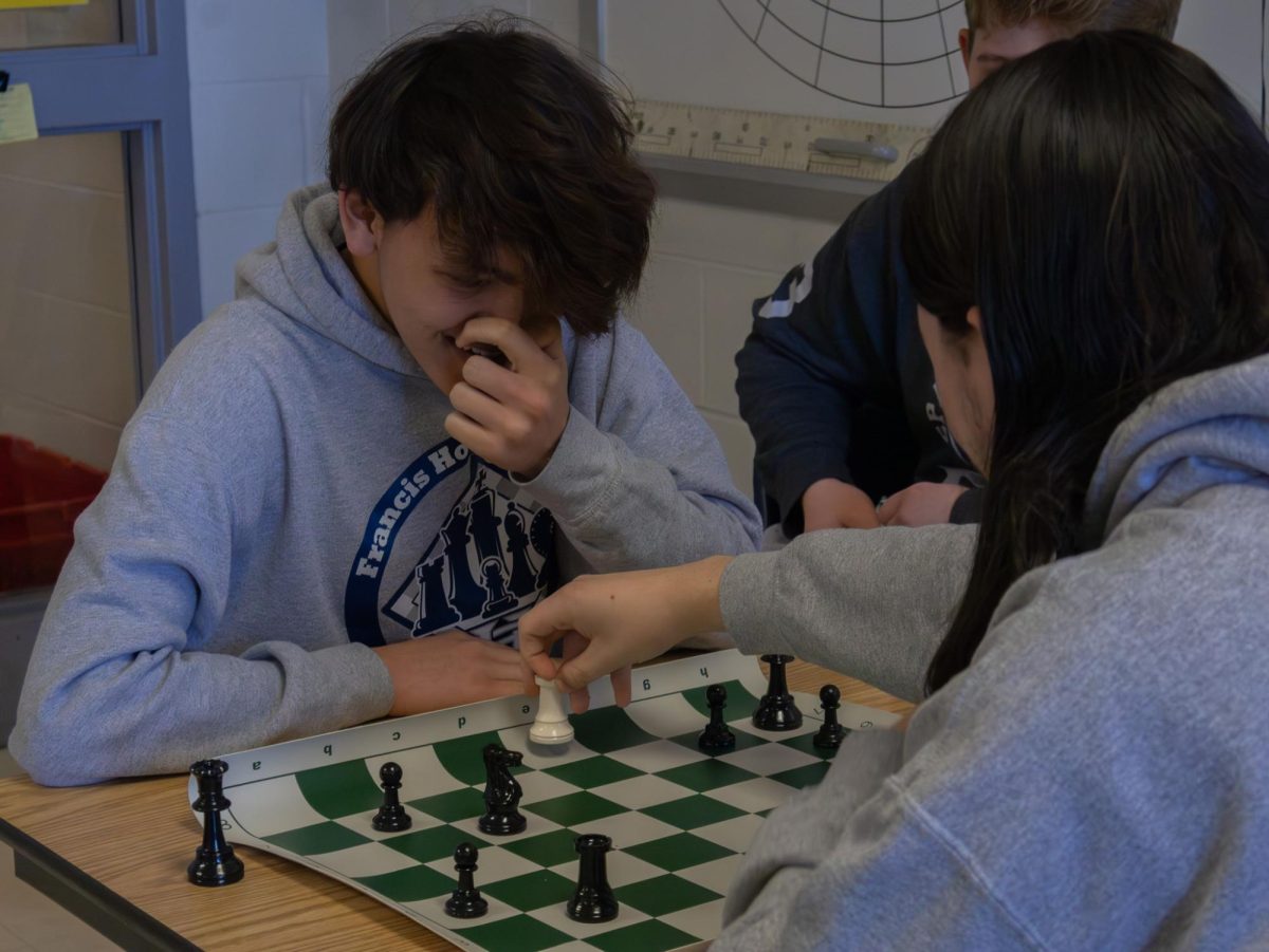 Junior Aiden Fraser laughs as senior Charlie Fussell moves his rook in their chess game. Many spectators watched the game play out, echoing the friendly community the chess club created.