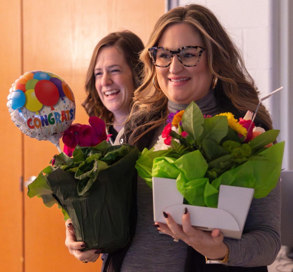 Mrs. Lentz smiling and holding flowers after being awarded the 2025 Teacher of the Year award. Mrs. Fry is beside her laughing and smiling while holding a balloon in celebration.