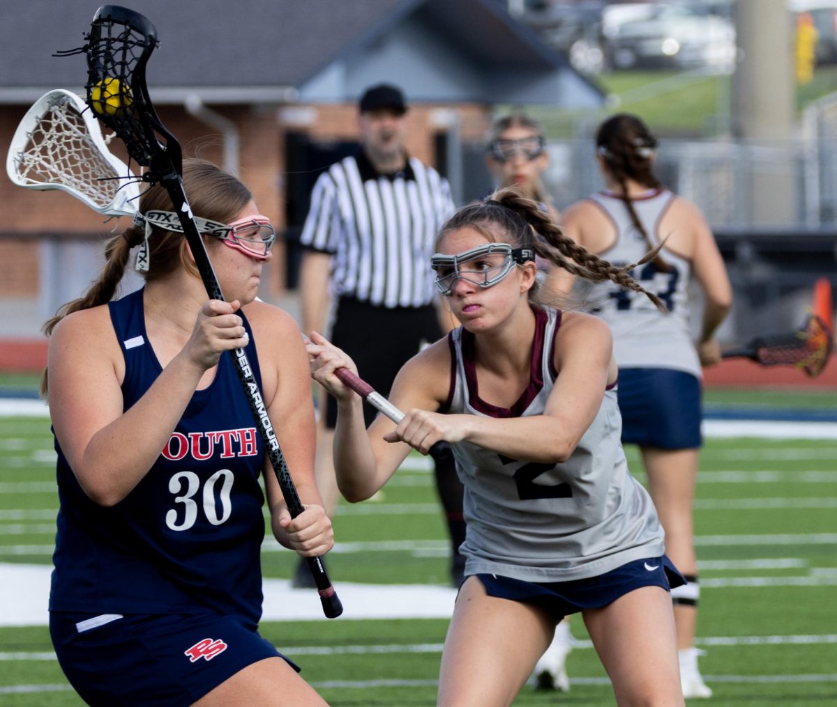 With her stick extending past the opposing player's head, Addison Holtgrewe sweeps the stick towards the ball in the opponent's possession. Holtgrewe’s aggressive actions towards defense acquired the ball for the team. 
