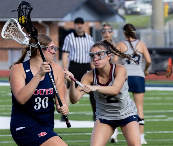 With her stick extending past the opposing player's head, Addison Holtgrewe sweeps the stick towards the ball in the opponent's possession. Holtgrewe’s aggressive actions towards defense acquired the ball for the team. 
