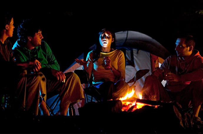 As they sit around a campfire, a woman holds a flashlight under her face while she recites scary stories and her friends cower in fear.  Scary stories are most often told in the dark, before bedtime, to create an unsettling ambiance.