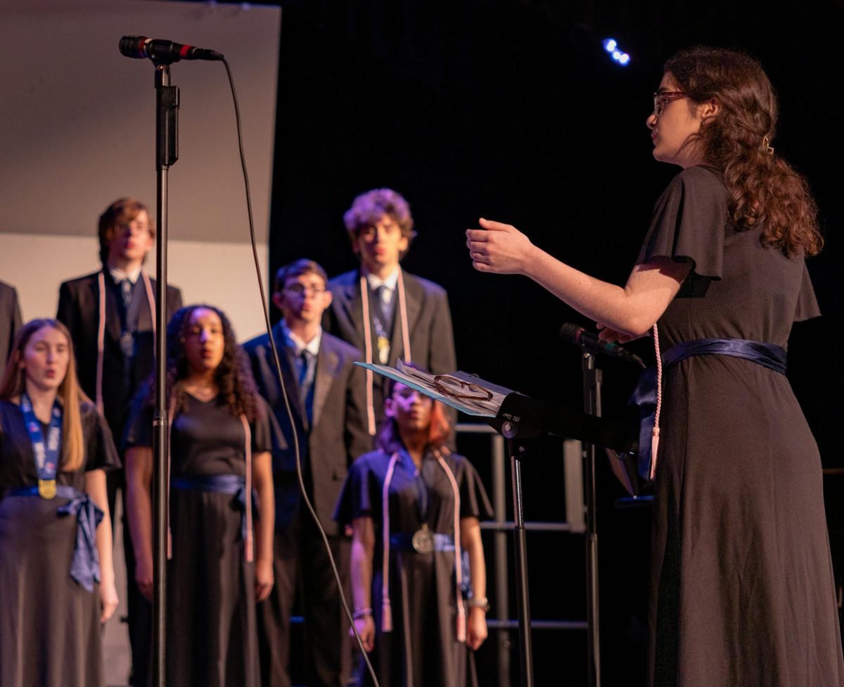 Conducting the Chamber Choir during its final performance on May 12, senior Katie Garrett motions to the singers of her arrangement of Lizzy McAlpine's "Give Me A Minute." Garrett is the first student in the choir program's history to arrange a song for the choirs to perform. 