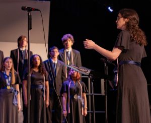 Conducting the Chamber Choir during its final performance on May 12, senior Katie Garrett motions to the singers of her arrangement of Lizzy McAlpine's "Give Me A Minute." Garrett is the first student in the choir program's history to arrange a song for the choirs to perform. 