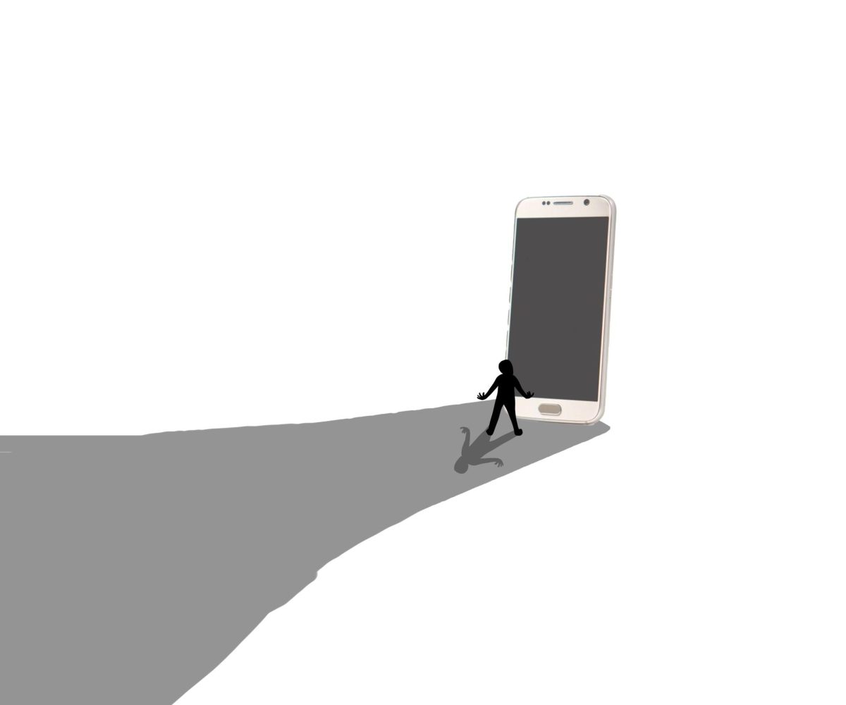 A person stands beside a large phone towering over them, overshadowing their own shadow. Technology is helpful but can sometimes become a detriment when used in excess. Photo Illustration by Birdie Brereton