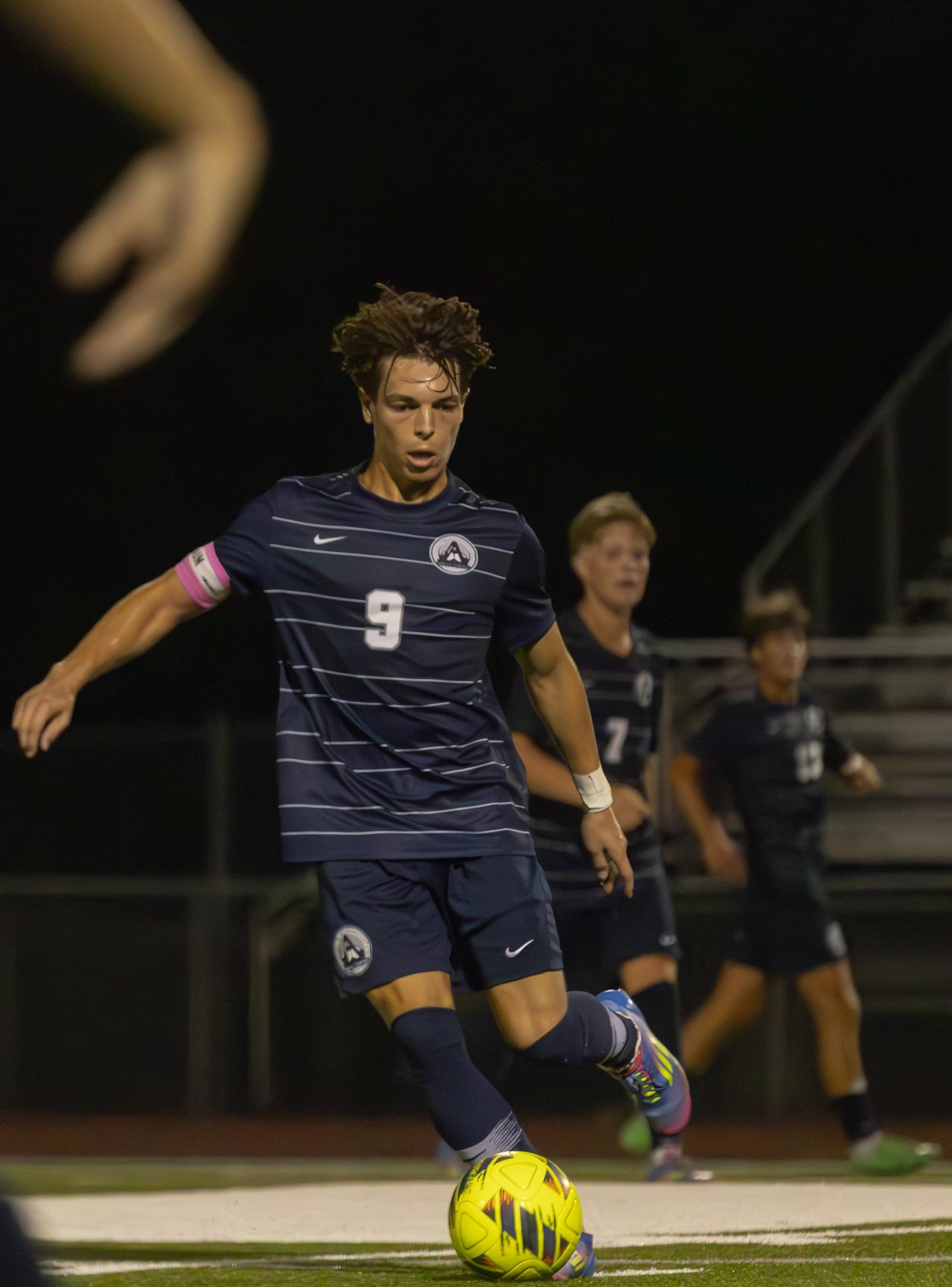 Tactfully maneuvering the soccer ball around others, senior Dominic Gianino begins to pass the ball to his colleague. The athlete reaches his leg back to generate enough force to kick the ball in the intended direction.