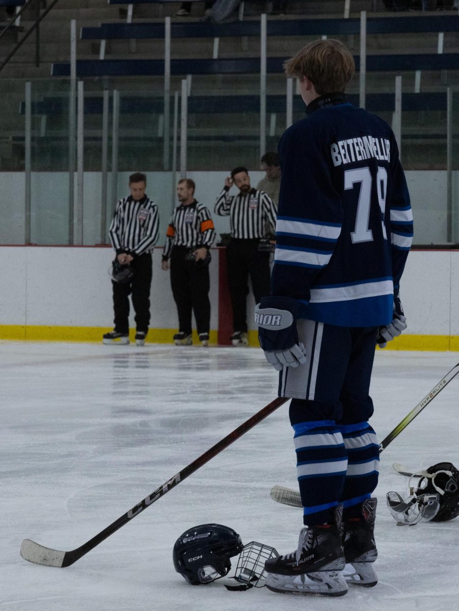 Standing on the ice during a moment of silence, junior Carson Bextermueller looks out to the other team. This game was a memorial for a student who lost his life at East.
