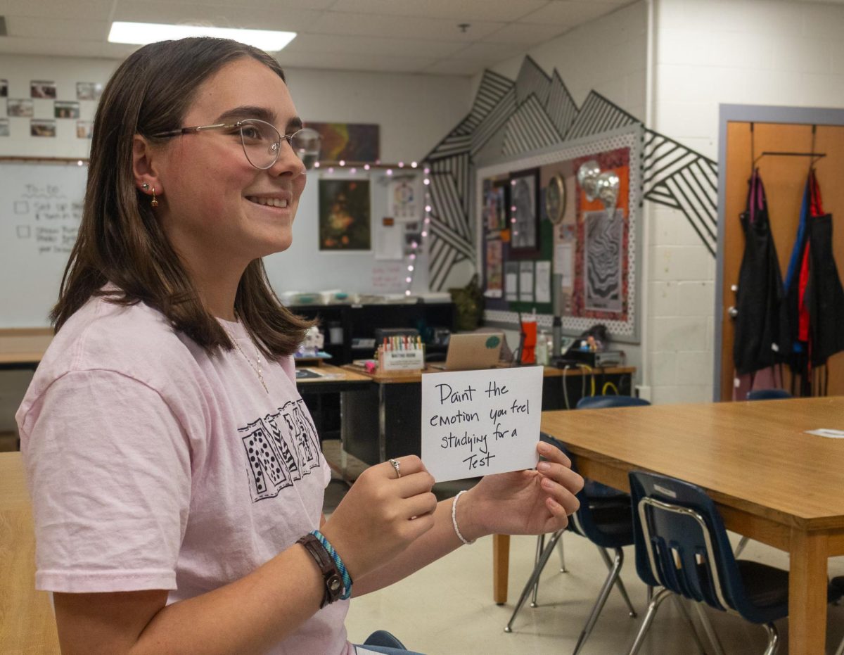 NAHS president, senior Olivia Dalton, draws a card and reveals the task the contestants must complete within 60 seconds. The contestants will have to use toothpaste to paint the emotion they feel when studying for a test on Nov. 10.