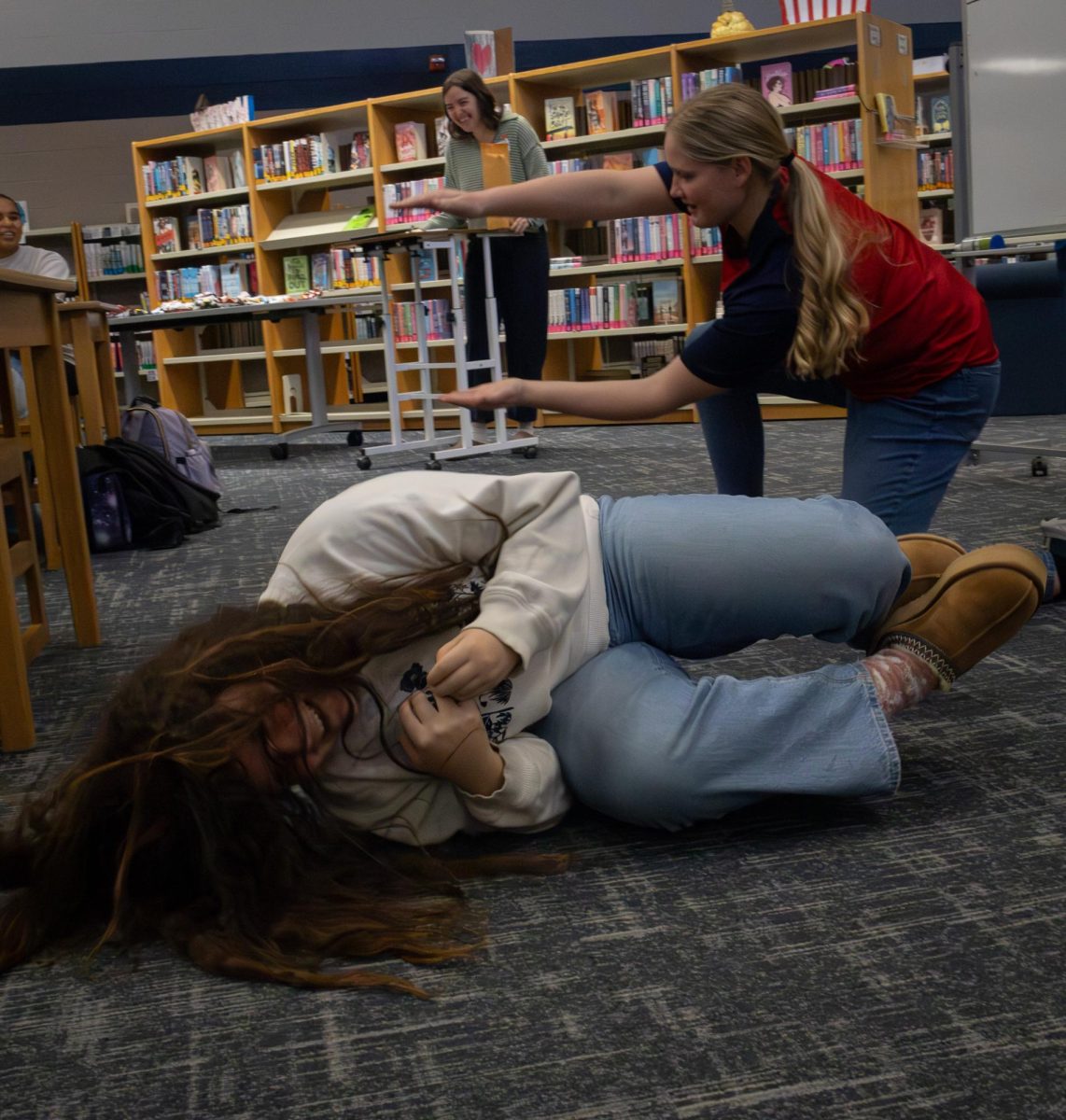 While acting out the word “sneaking out a window,” freshman Brooke Muschler rolls on the ground in an attempt to convey getting out a window to the attendees of the book club on Dec. 10, while her friend, freshman Annika Olson, held her arms out as the window. Muschler's and Olson’s turn was full of laughter as people guessed their word.
