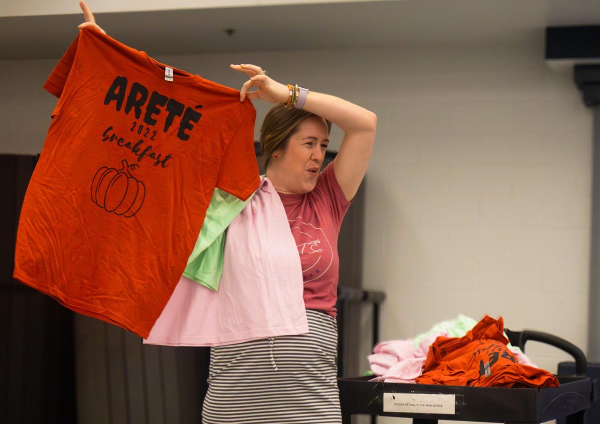 Mrs. Fetsch, an Algebra teacher, holds up Arete club t-shirts to the students at the Arete breakfast on Nov. 21. After running out of gift cards, she showed the students a replacement for the gift cards.
