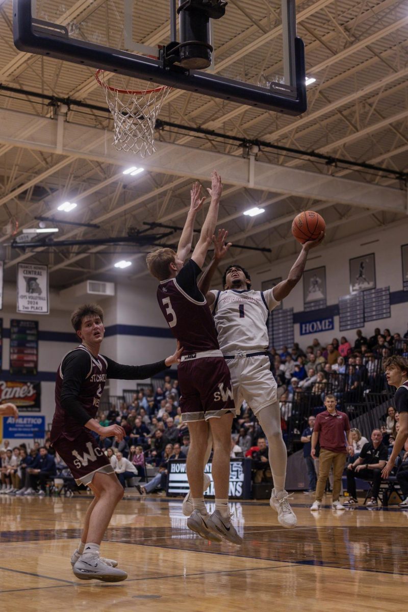 As a Saint Charles West Warrior reaches his arms up to hinder the shot, Xavier Morrison maintains connection with the ball as he prepares to send it into the hoop. Morrison successfully avoided the player’s block and scored another point on Jan. 20.
