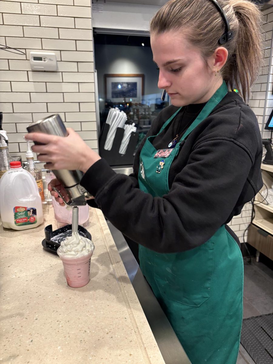 Junior Kinley Crane as she pours whipped cream on the Starbucks drink she has made with integrity. Crane works three or four days a week and has been working hard to balance this and school.