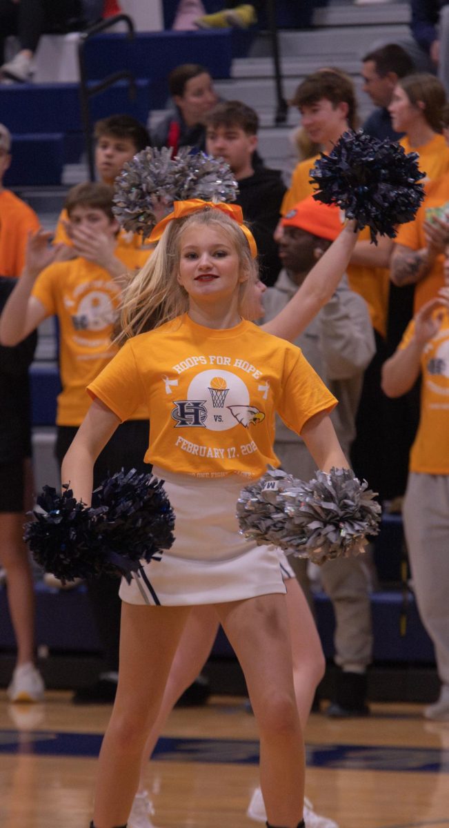The teams have requested a time-out, and the cheerleaders perform their short routine in the meantime. Freshman Maddie Callier moves her pom-poms to the beat of the dance on Feb. 17.